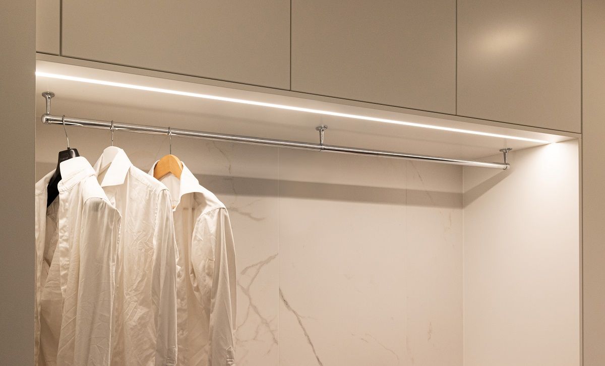 Led strip lighting in recessed aluminium profile with neutral light colour temperature on the top of an open wardrobe.